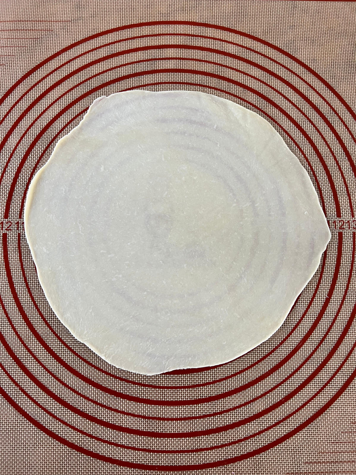 A sourdough tortilla is shown rolled out on a baking mat. 