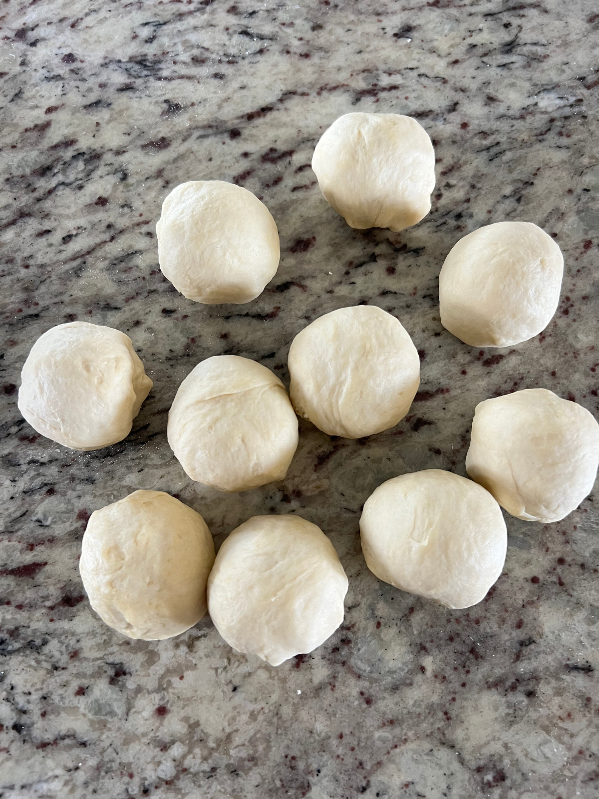 Ten sourdough discard dough balls sit on the counter preparing to be rolled out into tortillas.