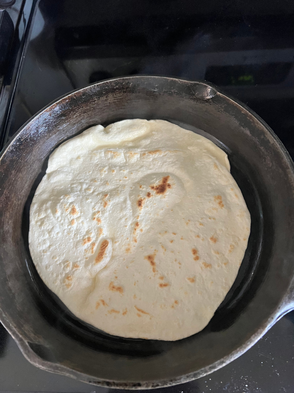 The sourdough discard tortilla is shown cooking on a cast iron skillet. 