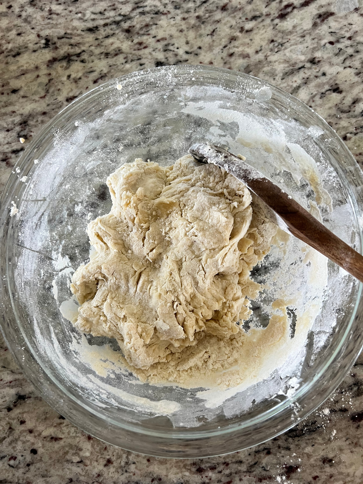 A glass mixing bowl holds the shaggy sourdough tortilla dough that will get kneaded into a ball. 