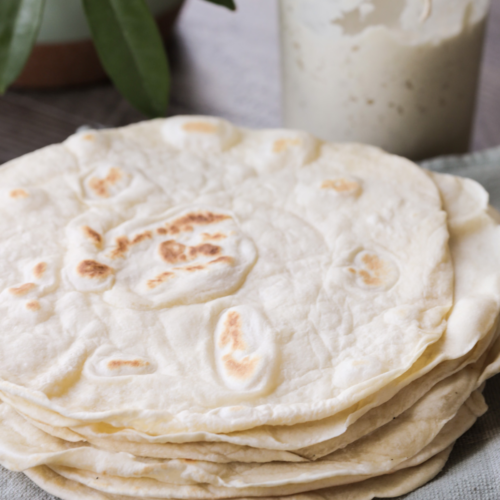 A stack of soft sourdough discard tortillas rest on top of a plate.
