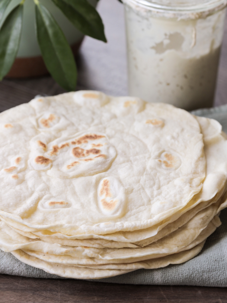 A stack of soft sourdough discard tortillas rest on top of a plate.