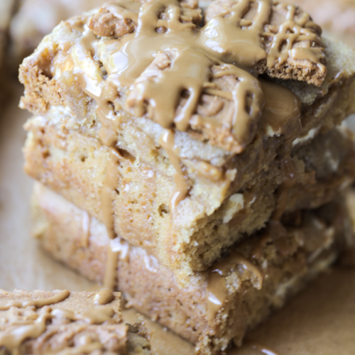 Three sourdough discard brown butter Biscoff blondies are shown stacked with a drizzle of Biscoff cookie butter over the tops of them.