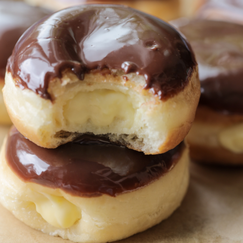 Naturally fermented sourdough Boston cream donuts--one stacked on another. The top donut has a bite taken out of it so you can see the homemade vanilla custard inside.