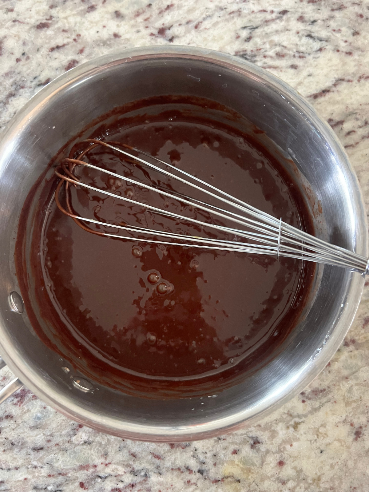 The chocolate ganache is shown in a saucepan with a whisk in it. The sourdough donuts will be filled with custard and then dipped in the chocolate ganache.