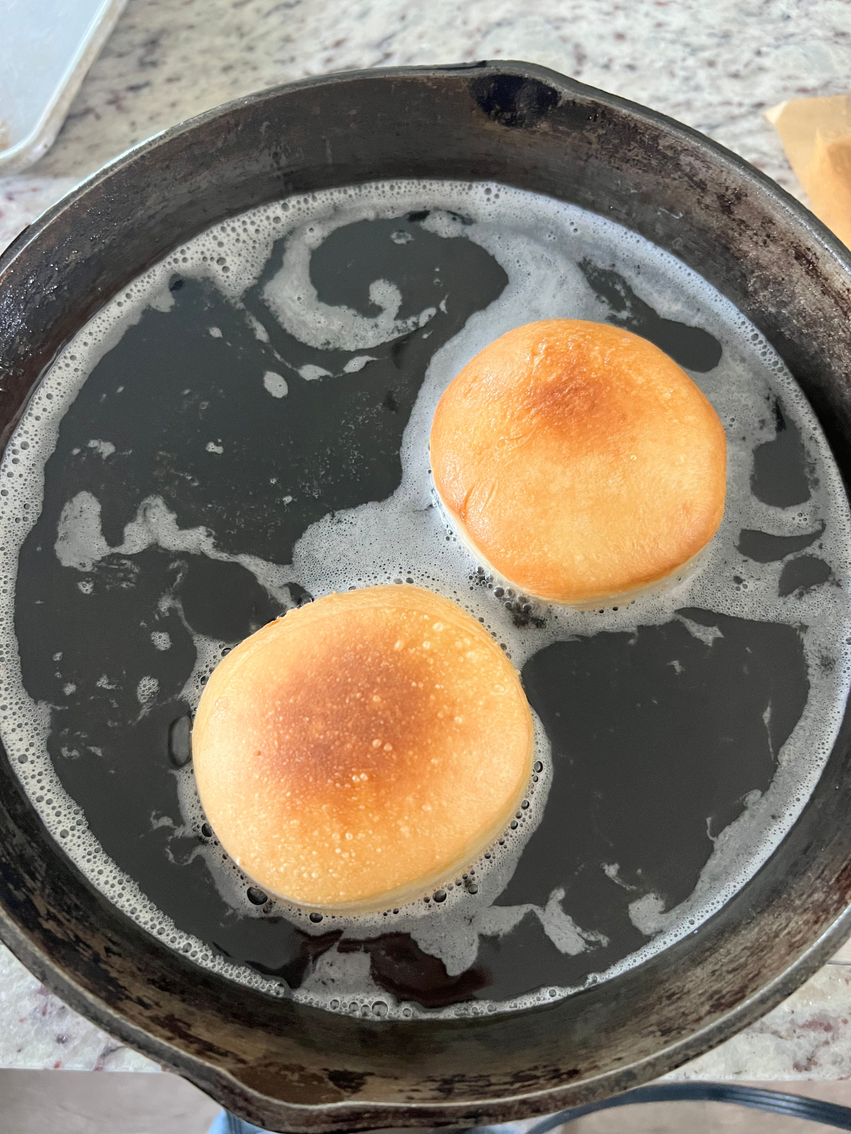 The sourdough donuts are shown golden brown and frying on the other side in the pan.