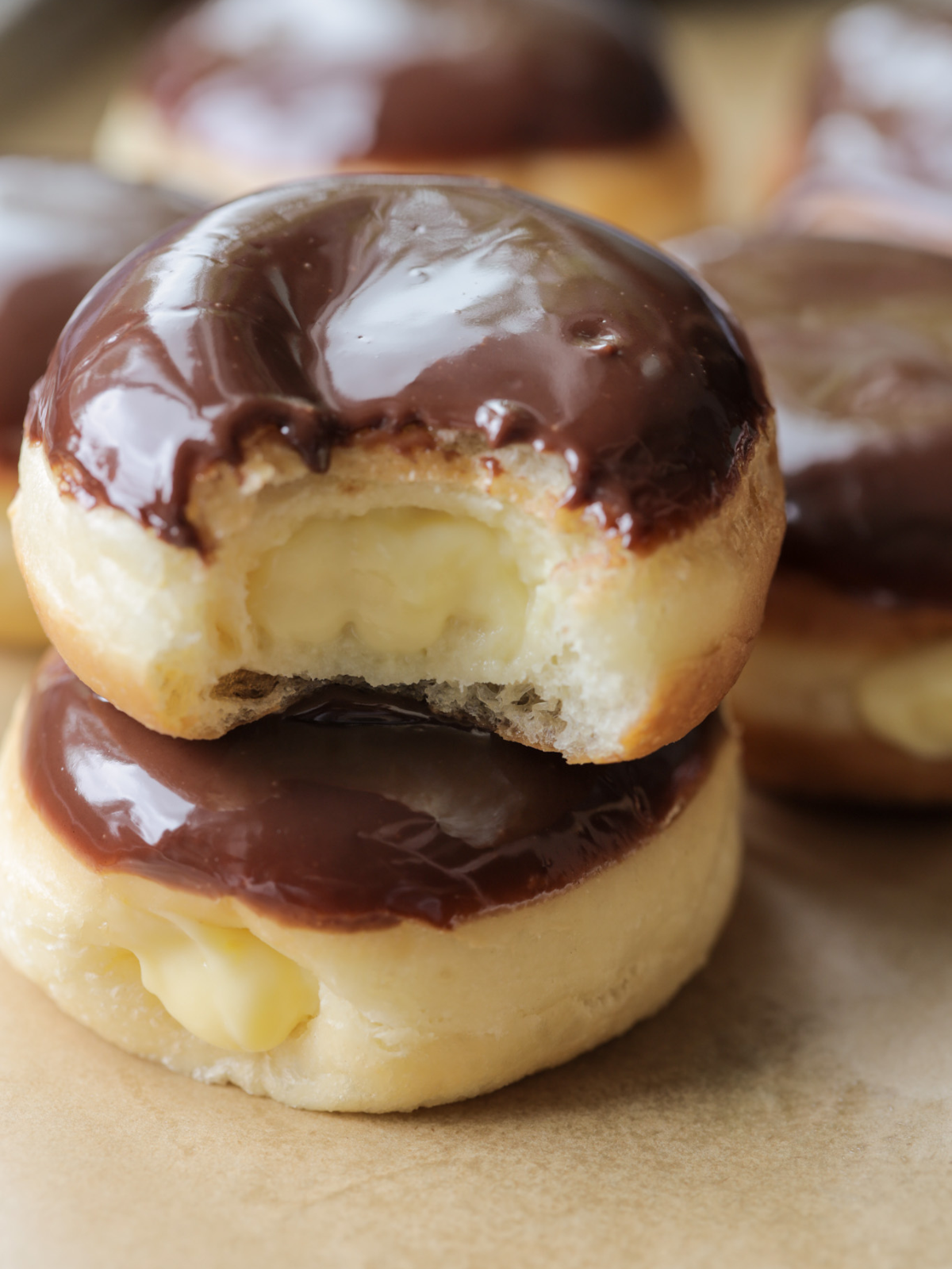 Naturally fermented sourdough Boston cream donuts--one stacked on another. The top donut has a bite taken out of it so you can see the homemade vanilla custard inside.