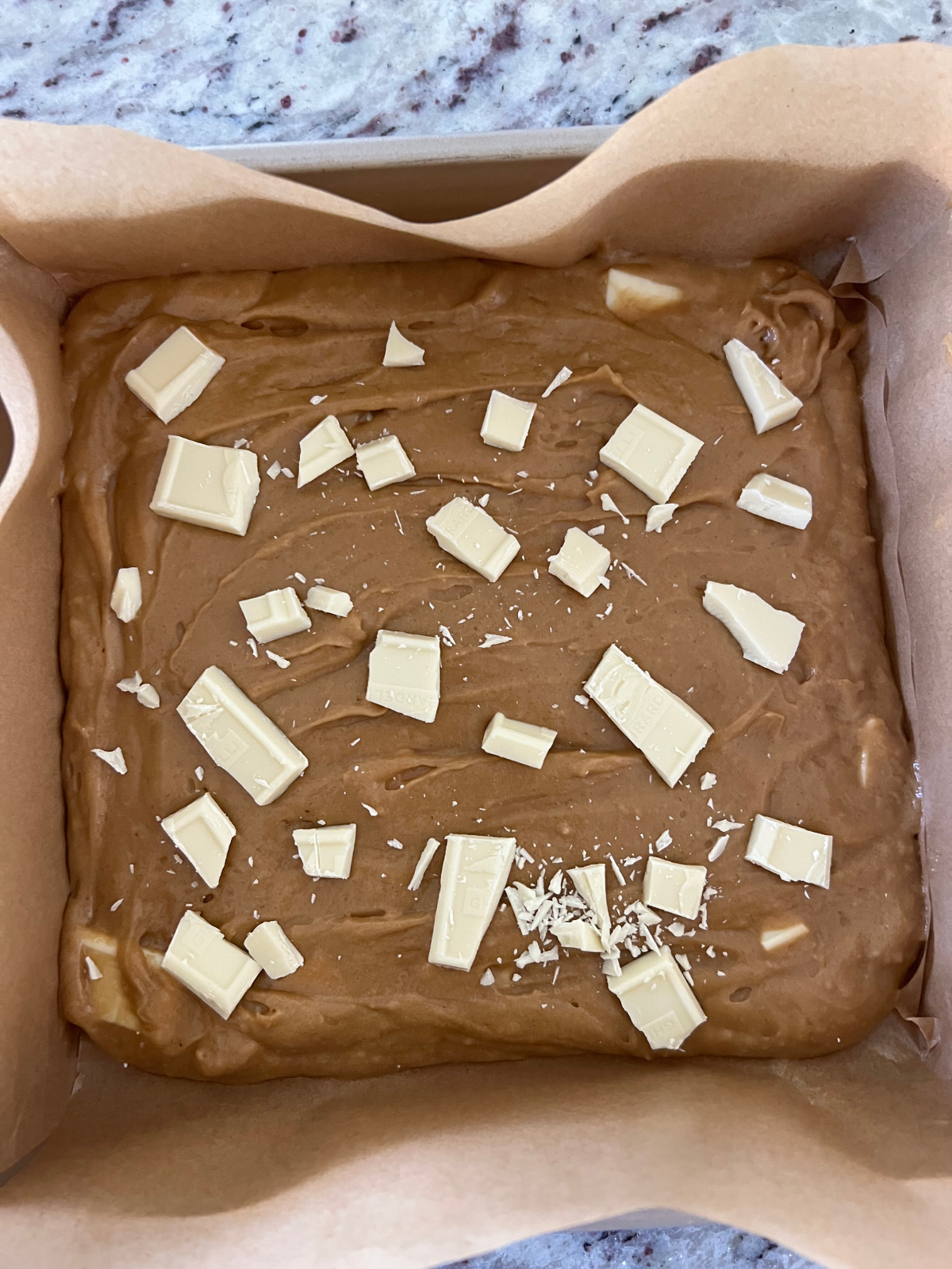 The batter for the sourdough discard Biscoff blondies are shown with chopped white chocolate sprinkled over them. They will be baked and then the cookies will be added.