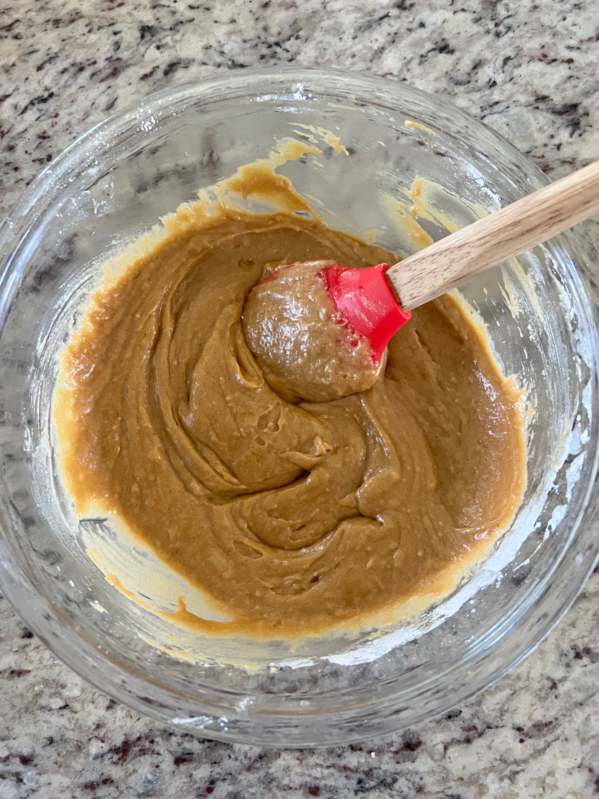 The batter for the brown butter sourdough biscoff blondies are shown in the glass mixing bowl with a rubber spatula in it.
