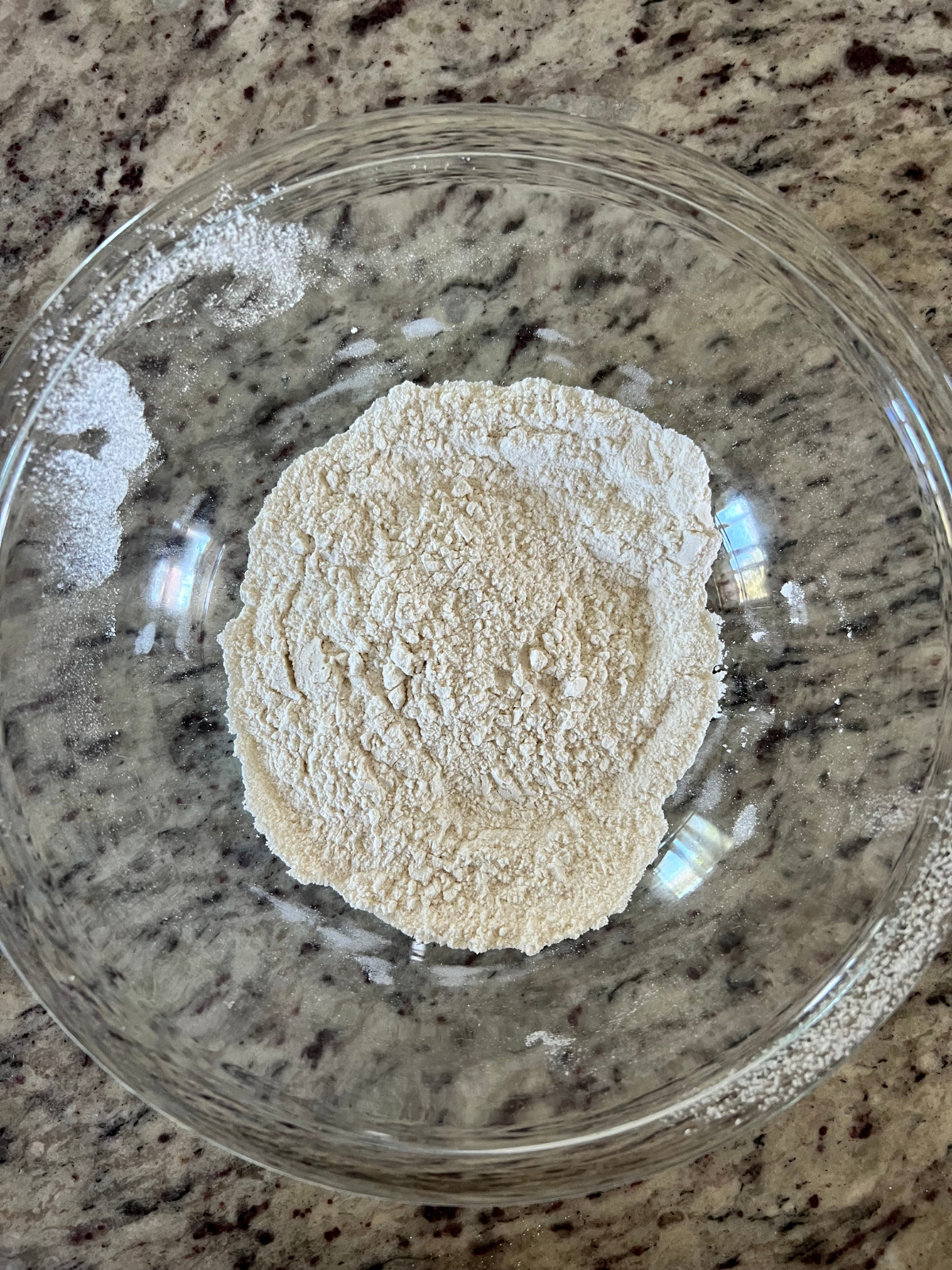 The flour, baking powder, and salt have been sifted together and are shown in a glass mixing bowl.