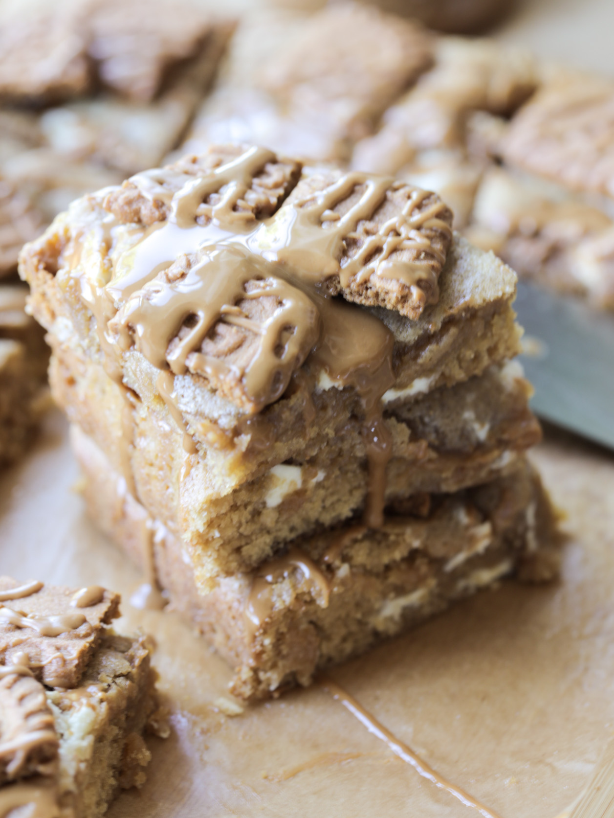 Three stacked sourdough discard Biscoff blondies are shown with Biscoff cookie butter drizzled over them and crushed Biscoff cookies on top.