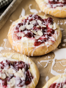 A closeup of a sourdough cream cheese bun with icing drizzled over it and several other sweet buns lay next to it.