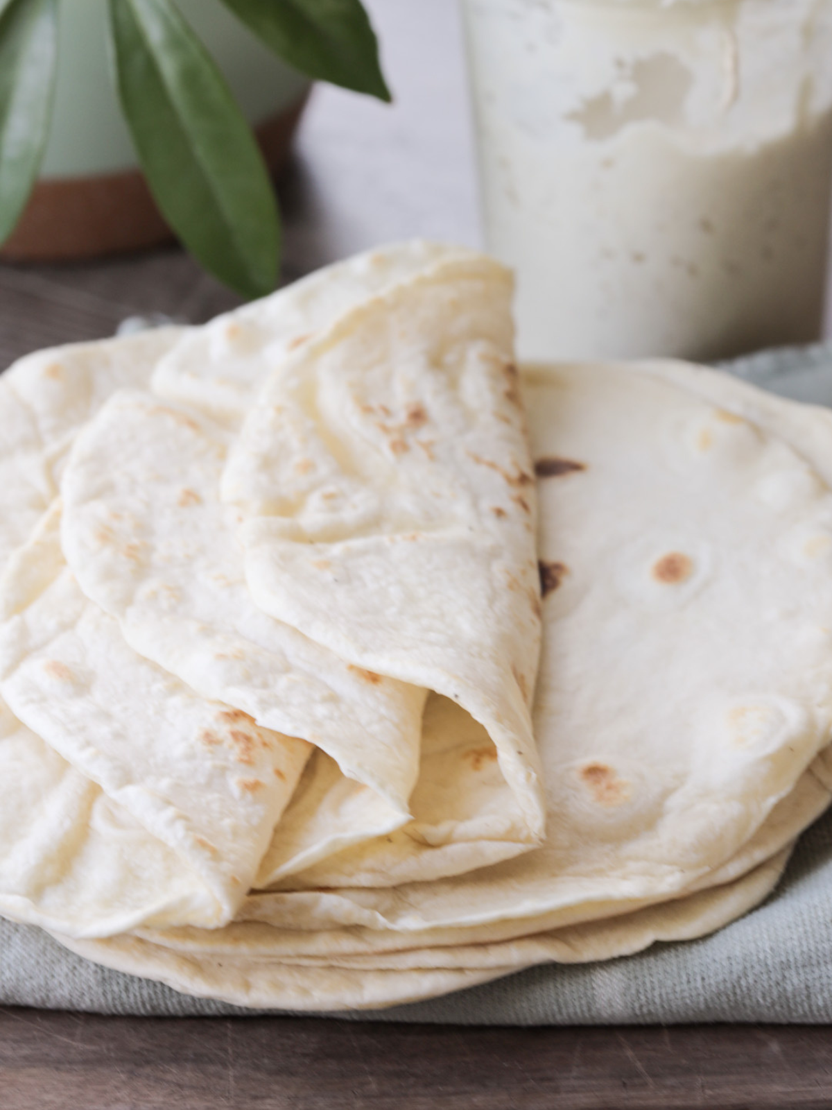 Three sourdough discard tortillas are shown flexibly soft and folded over and several more sourdough tortillas rest underneath them. 