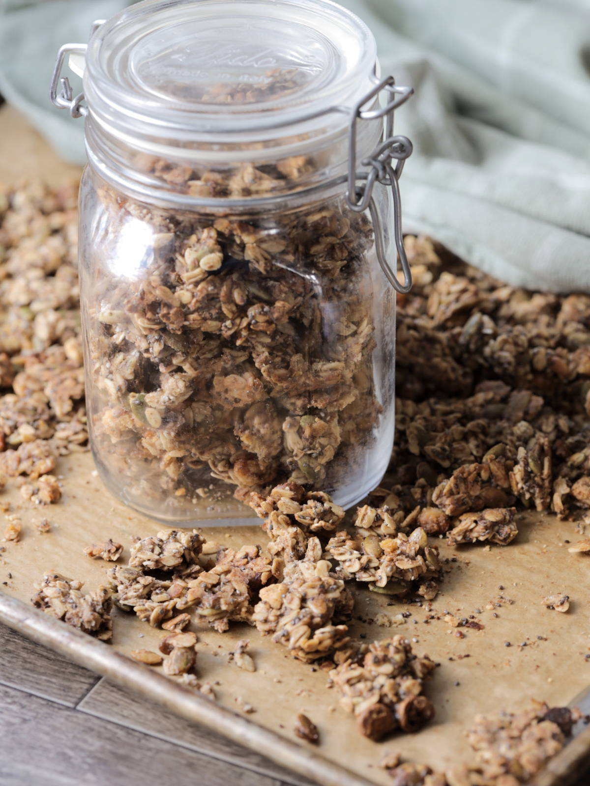 The sourdough granola sits in a glass jar with clusters of granola laying around the jar.