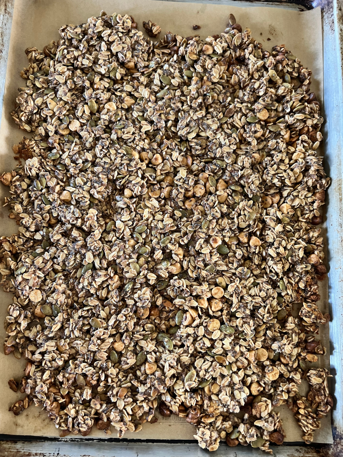 The sourdough granola is shown on the baking sheet after just being baked. It will cool and crisp up for a while before breaking into clusters.