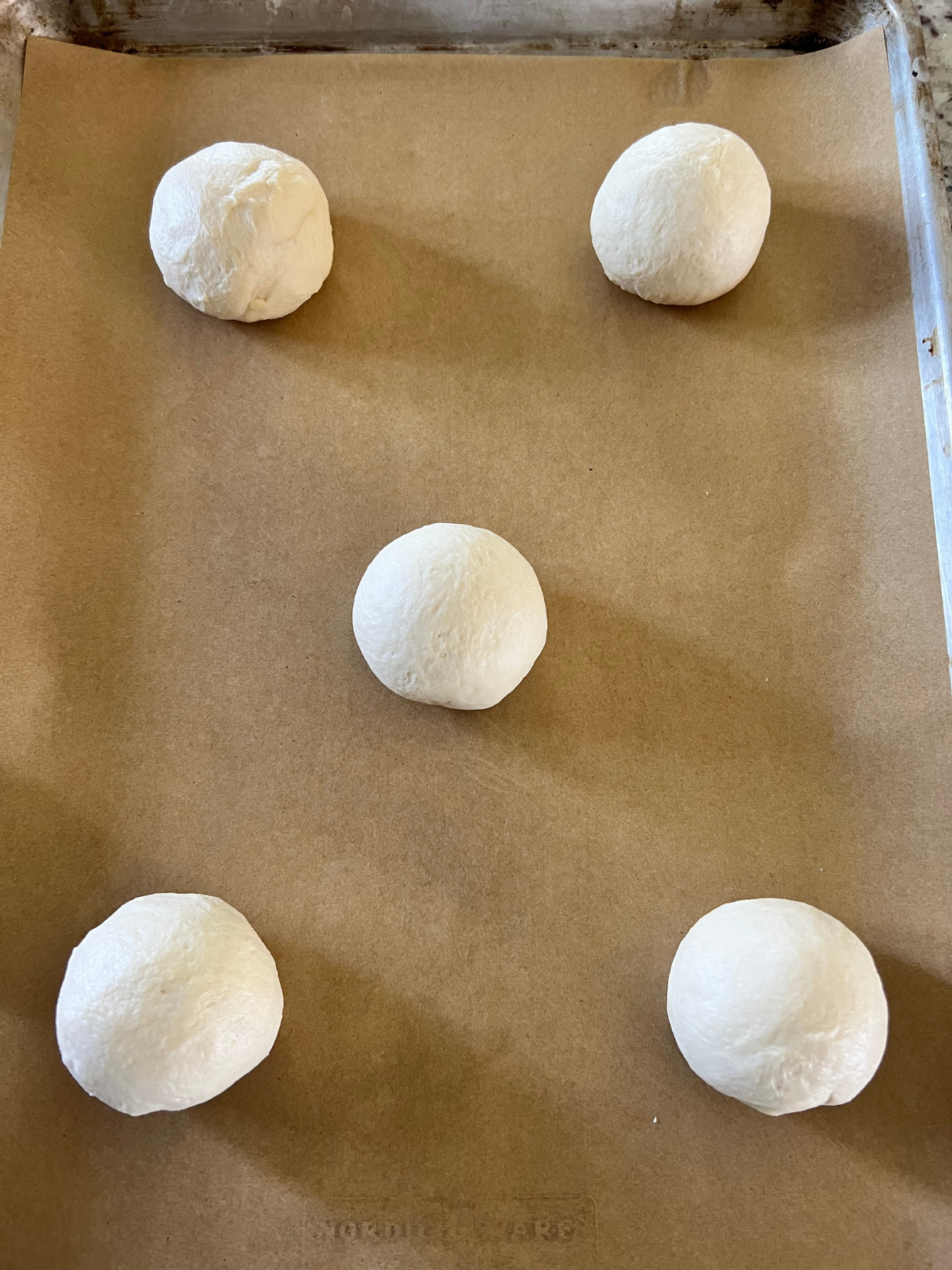Sourdough brioche lemon curd cream cheese bun dough balls rest on a parchment lined baking sheet preparing for their second rise.