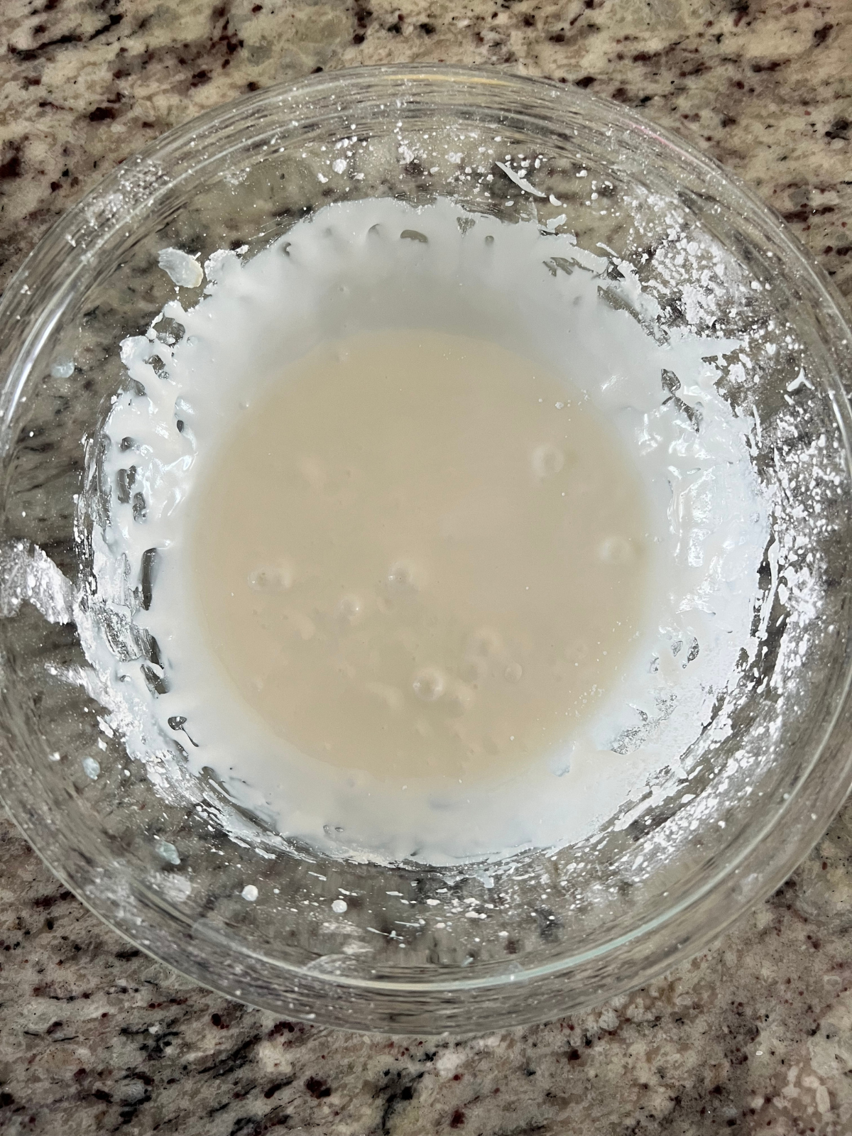 The icing sits mixed in a glass mixing bowl.