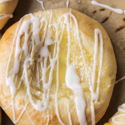 A closeup of a lemon curd cream cheese sourdough danish is shown with icing drizzled over it.