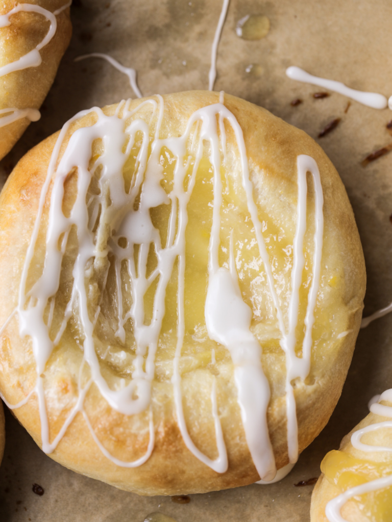 A closeup of a lemon curd cream cheese sourdough danish is shown with icing drizzled over it.