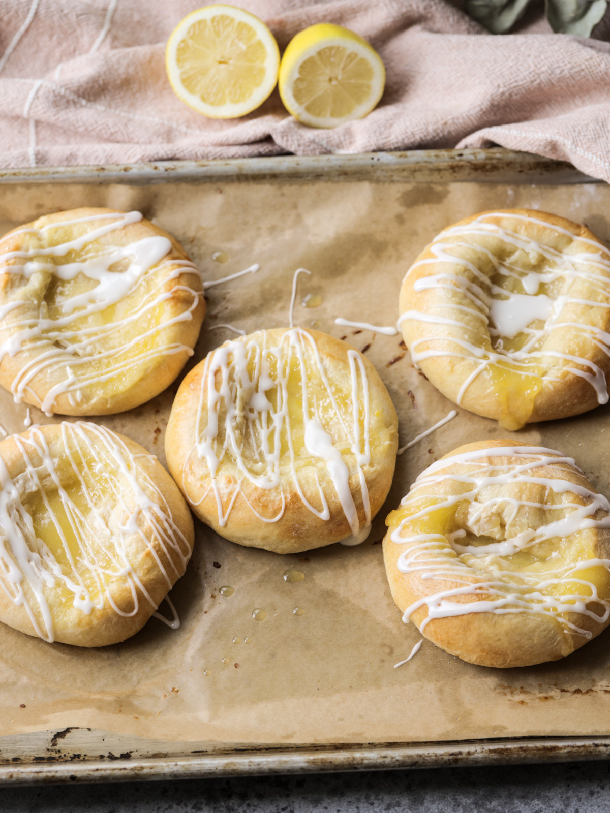 Five sourdough lemon curd cream cheese buns with icing sit on a parchment paper lined baking sheet.