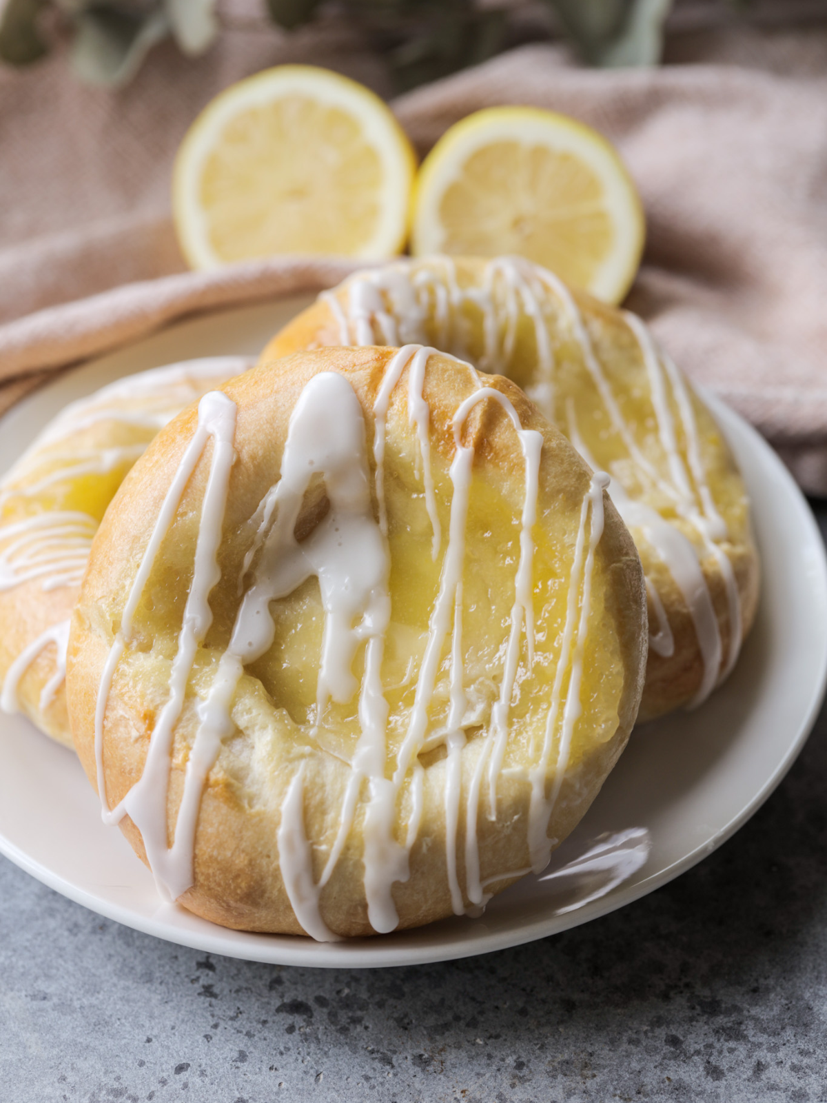 Three sourdough lemon curd cream cheese brioche buns with icing sit on a plate.