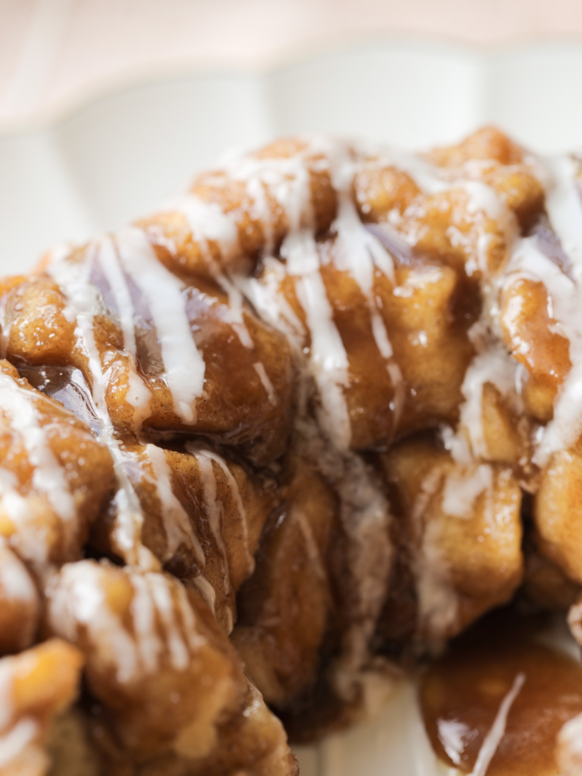 A closeup of the naturally fermented sourdough monkey bread with vanilla icing is shown on a serving plate.