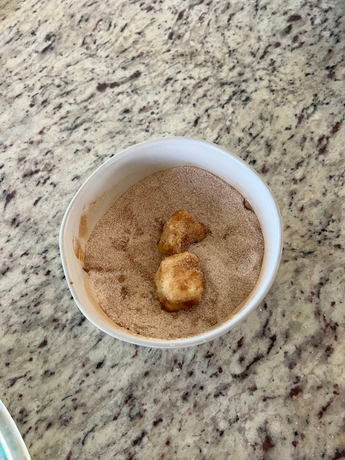 The sourdough dough pieces sit in a bowl of cinnamon sugar.