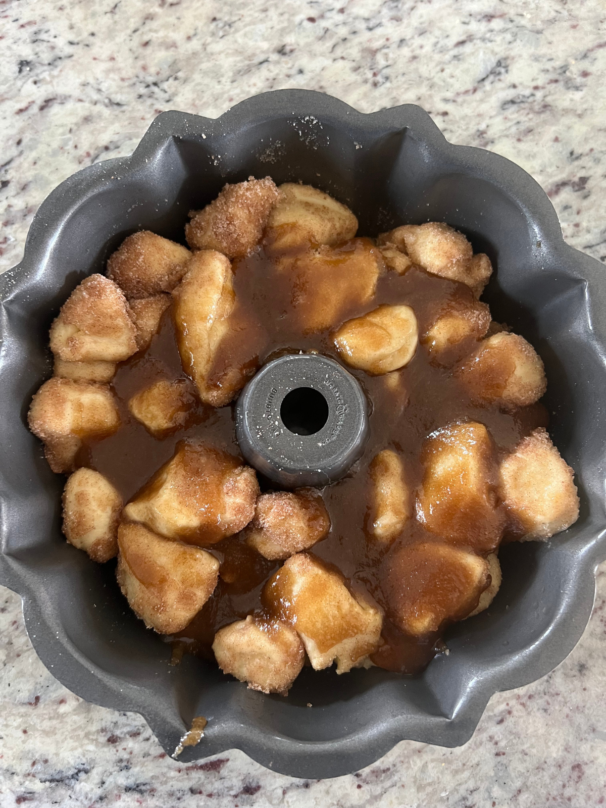 The sourdough monkey bread pieces sit in the Bundt pan after its second rise. The melted butter and brown sugar syrup has been poured over it.