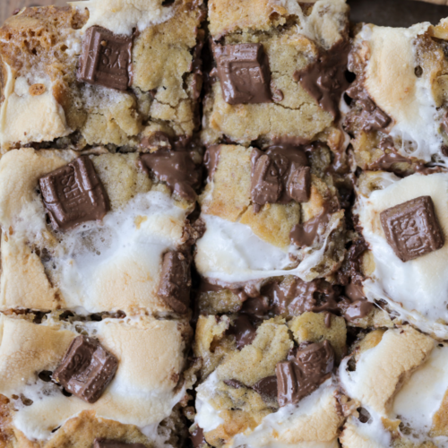 Sourdough s'mores cookie bars are shown with gooey marshmallows, melty chocolate bars crumbled over the top, and cut into squares ready to serve.