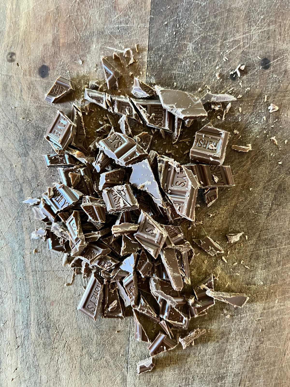 Hershey's milk chocolate bars are shown roughly chopped on a wooden cutting board.
