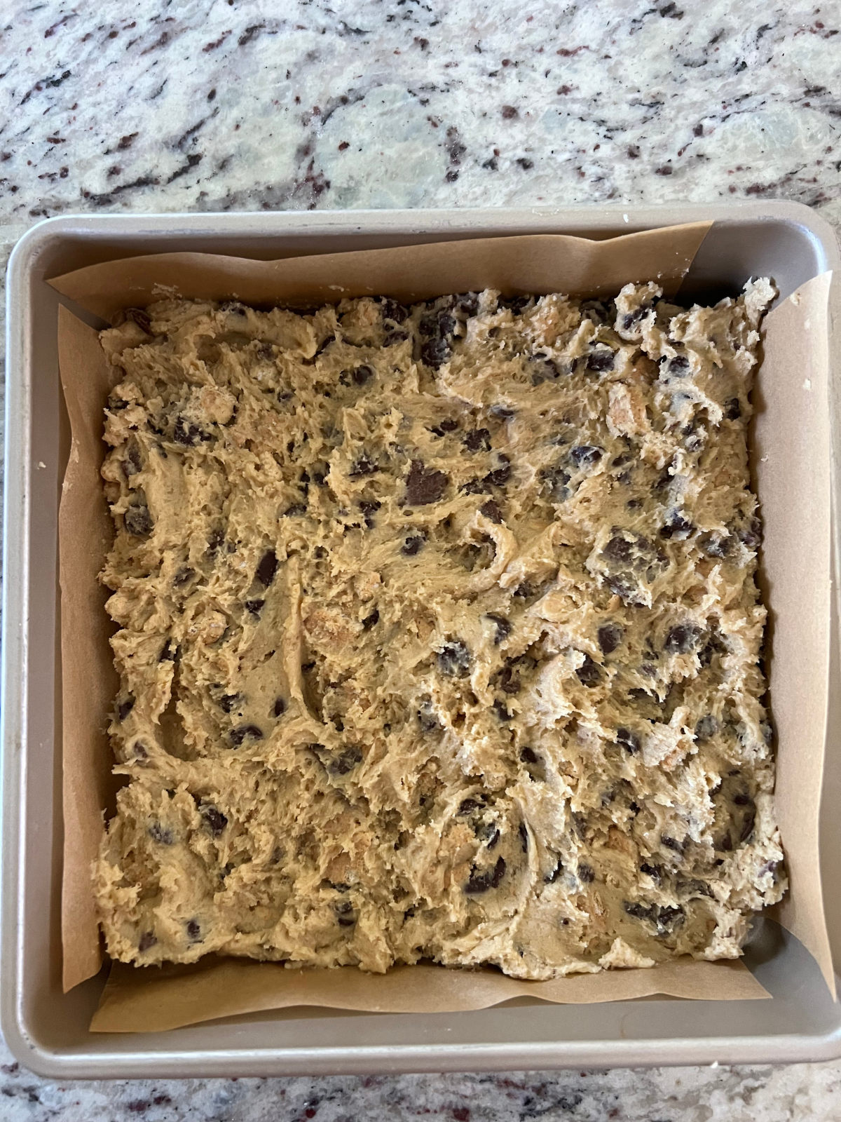 Two thirds of the sourdough s'mores cookie dough is pressed into a parchment paper-lined 9x9 baking pan.
