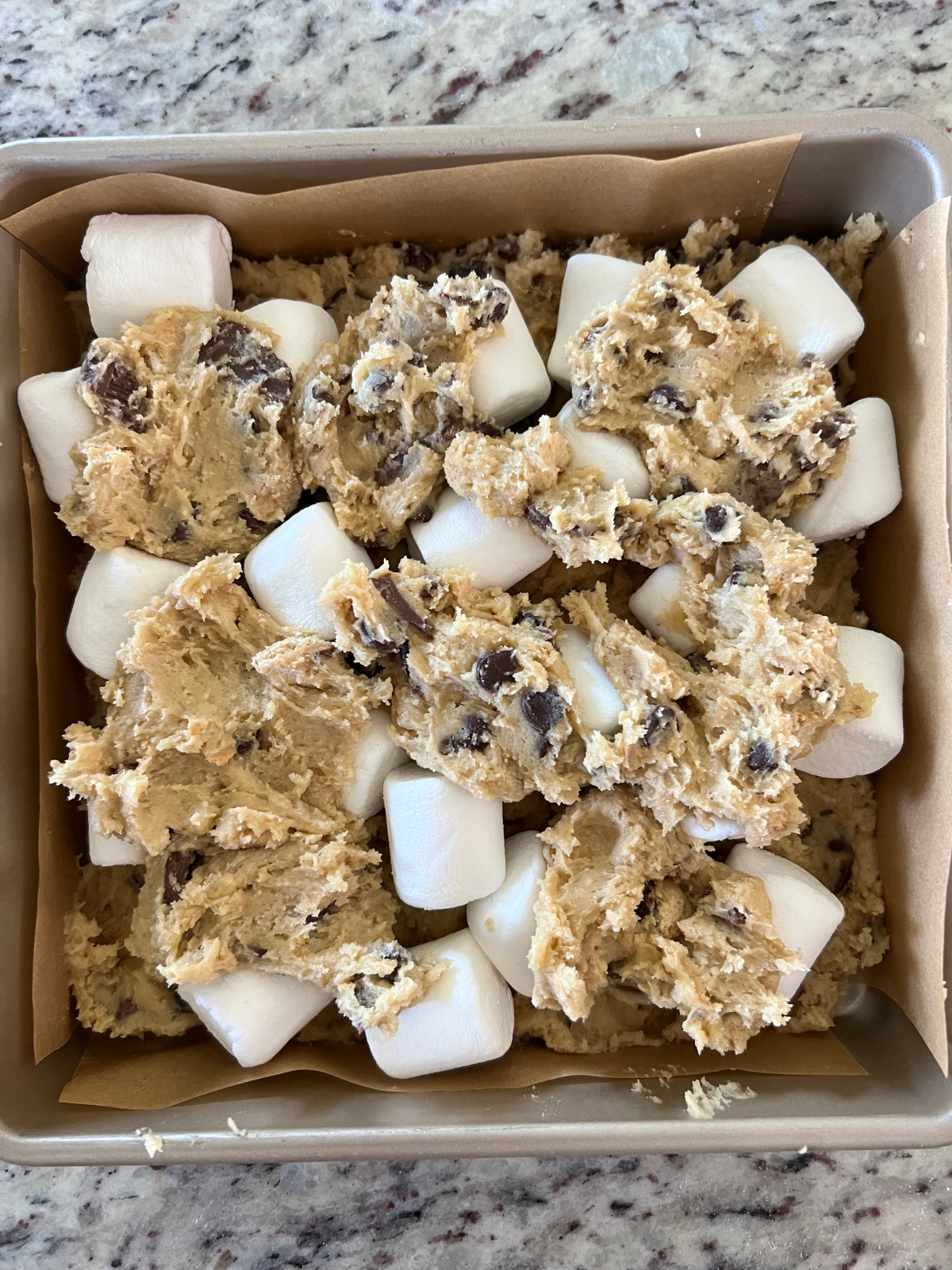 The remaining cookie dough is dropped over the marshmallows about to be baked.