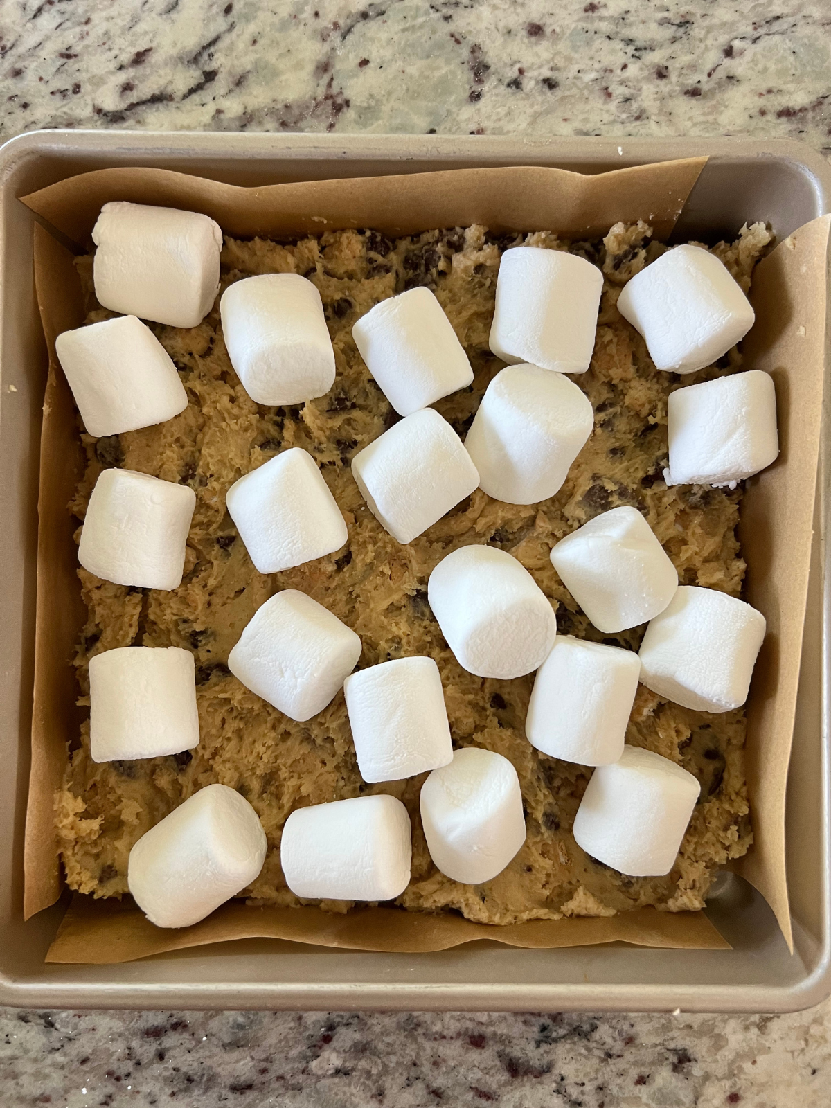 Regular sized marshmallows sit on top of the pressed down cookie dough in the baking pan.