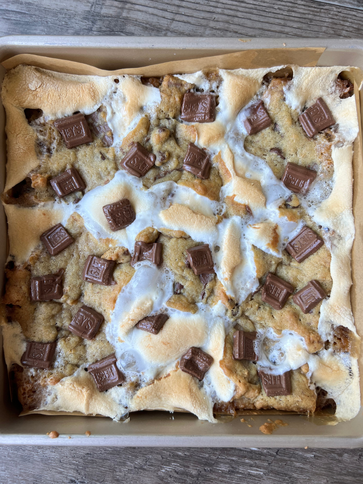 The freshly baked sourdough s'mores cookie bars sit in a 9x9 baking pan. The bars are golden brown with melty chocolate and toasted, gooey marshmallows.
