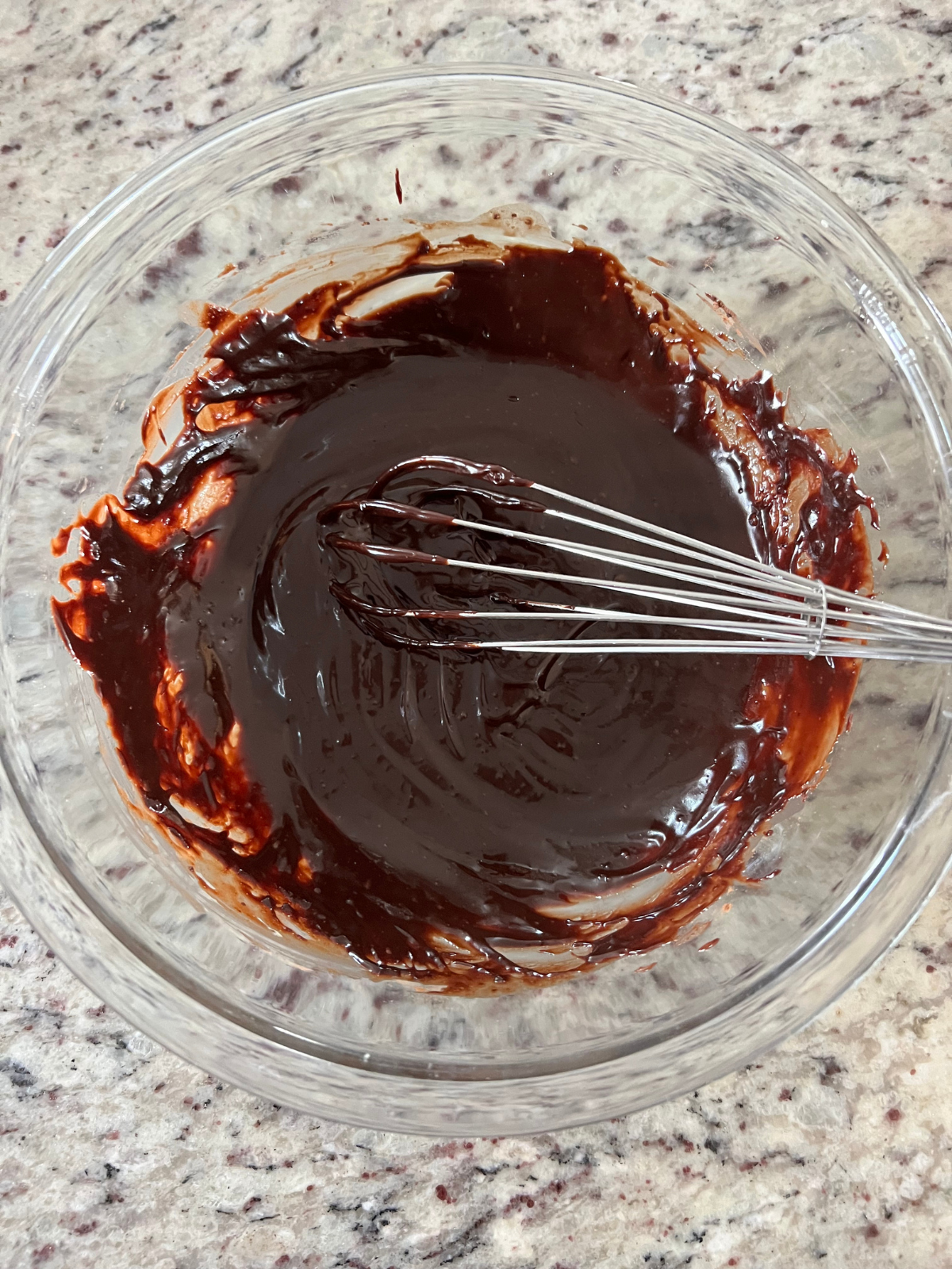 The chocolate ganache sits in a glass mixing bowl with a whisk in it.