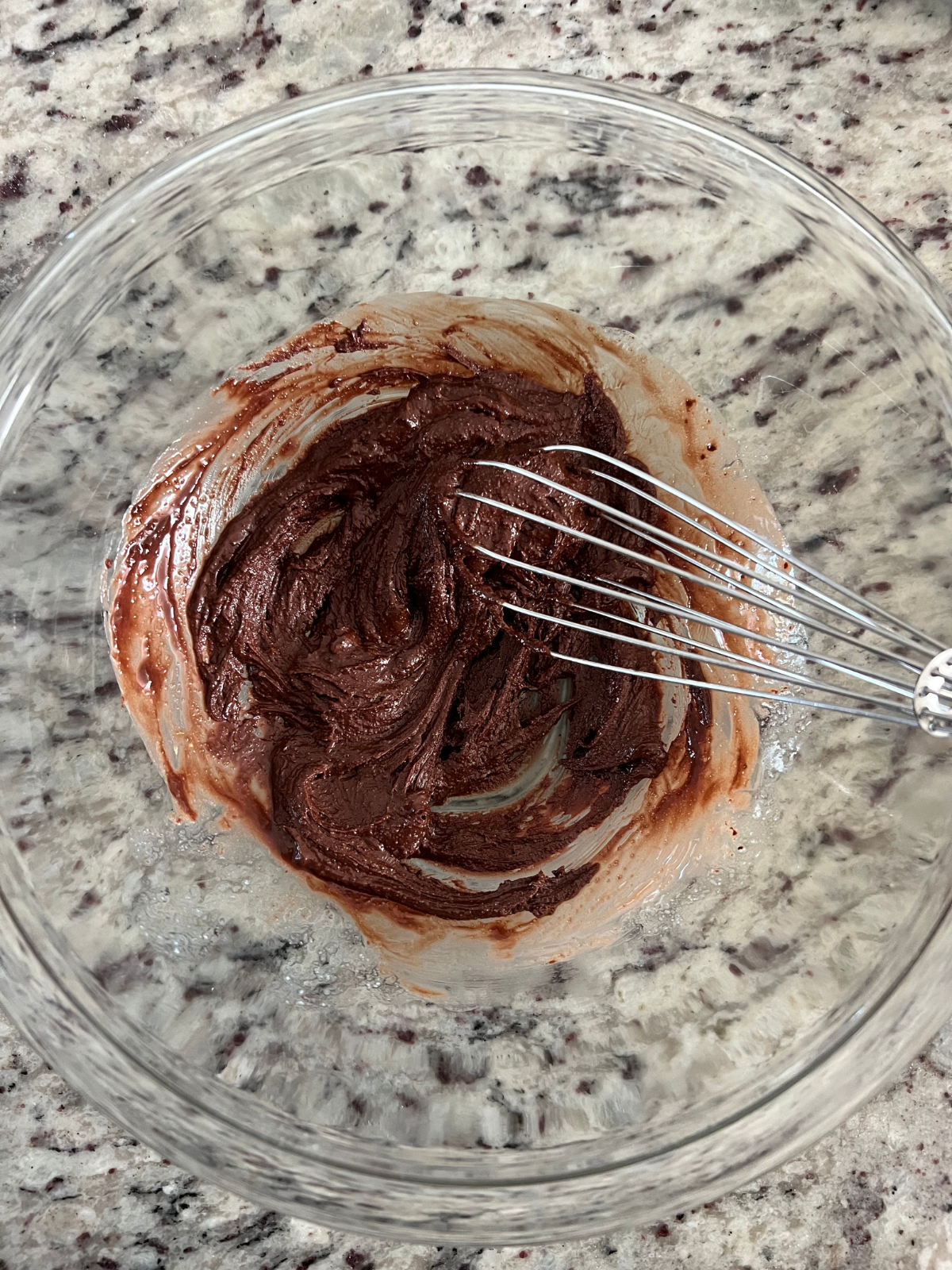 Chocolate icing sits in a glass mixing bowl with a whisk in the bowl. It will top the sourdough s'mores pop tarts. 
