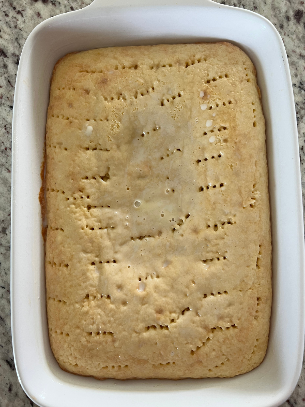 The sourdough tres leches cake is shown with holes poked in it and the milk soaked in.