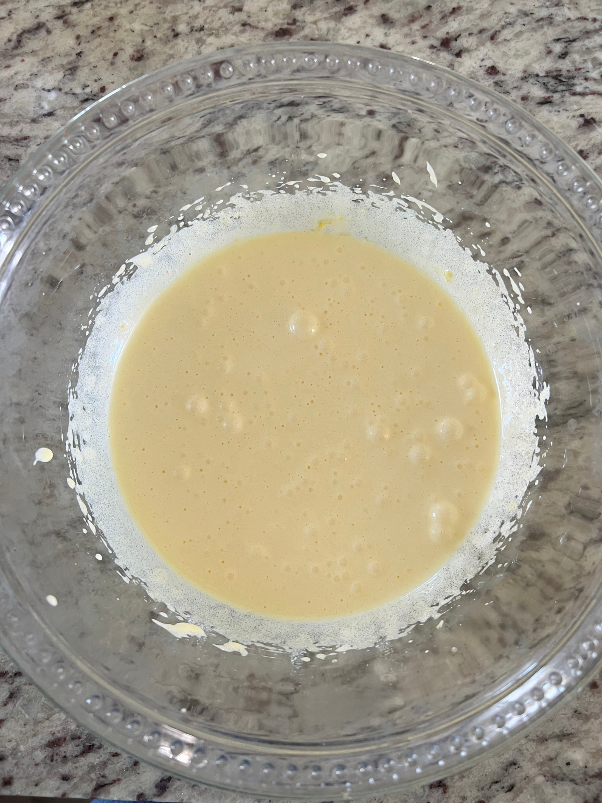 The egg yolks and granulated sugar have been beaten and rest in a mixing bowl.