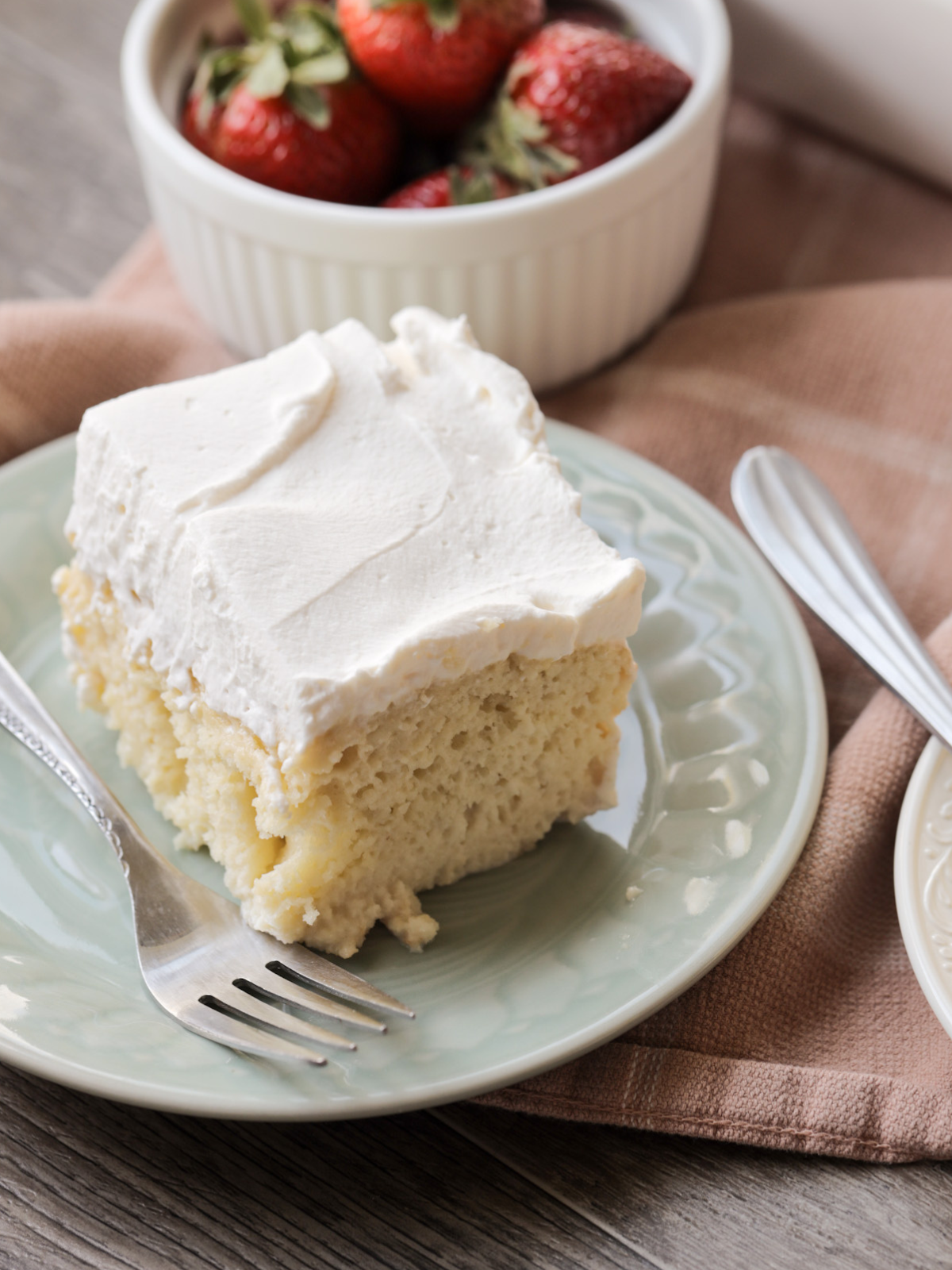 A slice of sourdough tres leches cake with whipped cream topping sits on a plate. 
