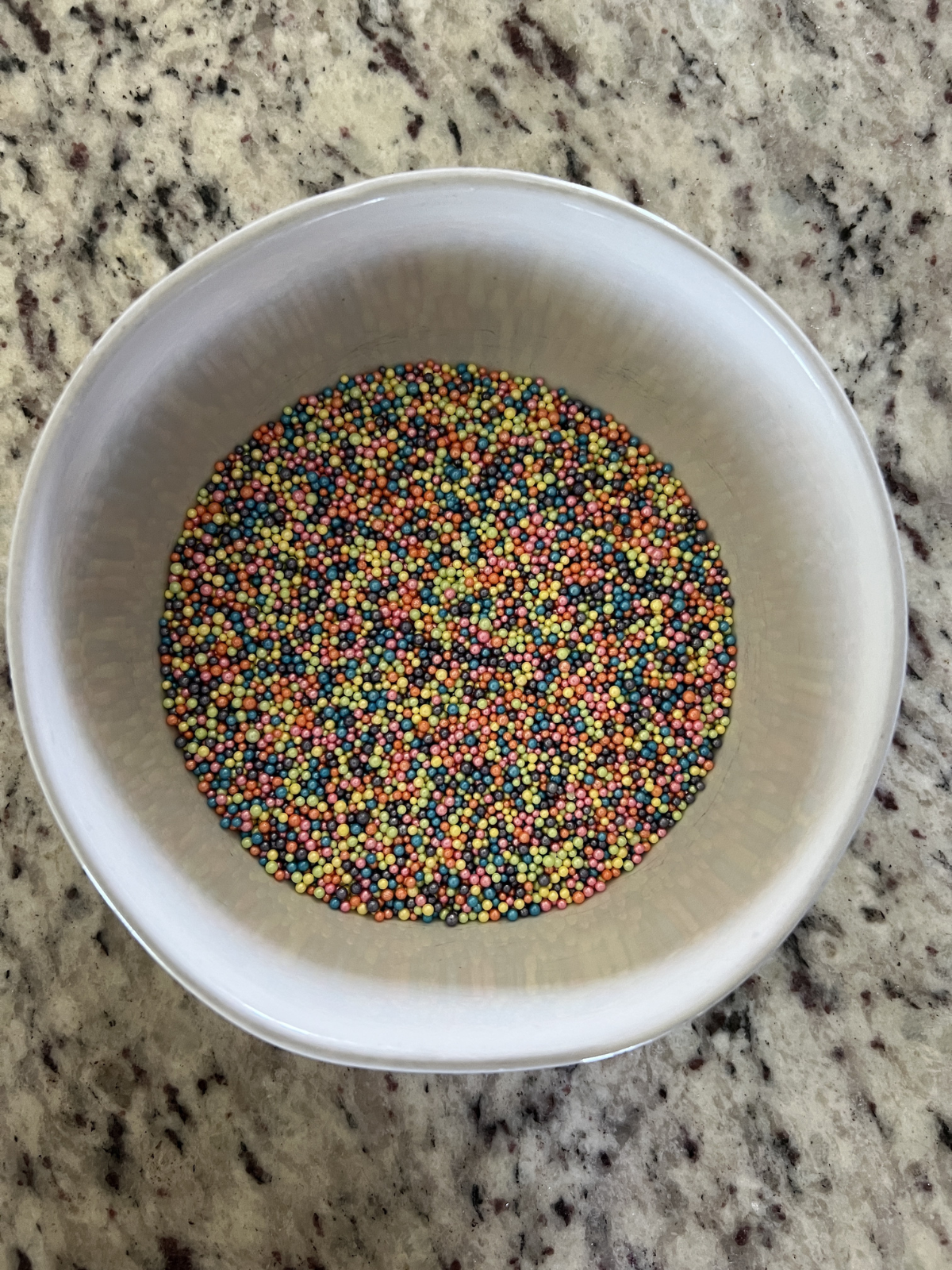 The nonpareils sprinkles sit in a small bowl. The cakes will be dipped upside down into the sprinkles.
