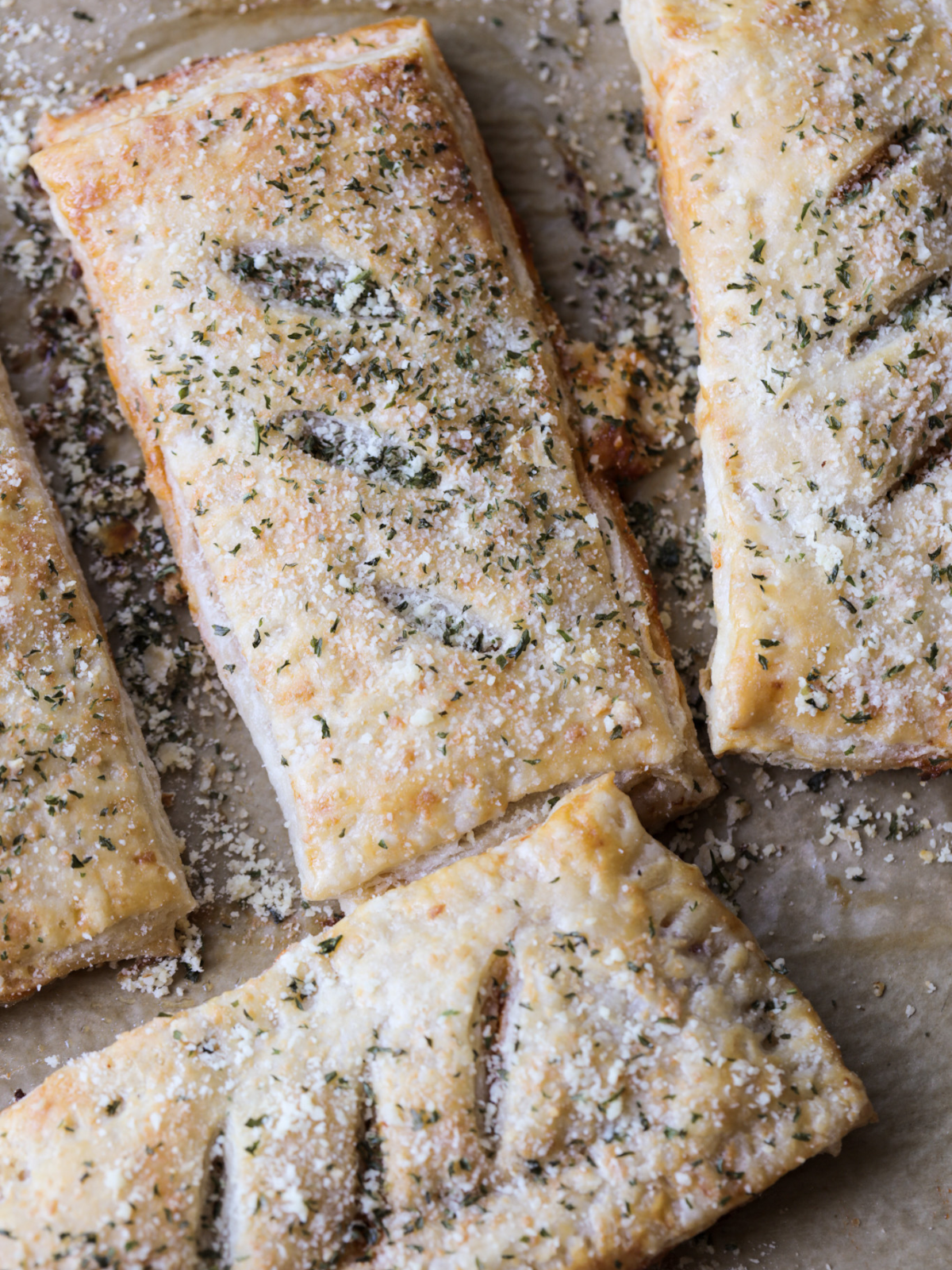 A close up of a few sourdough hot pockets with butter brushed on and topped with more grated parmesan cheese and dried parsley.