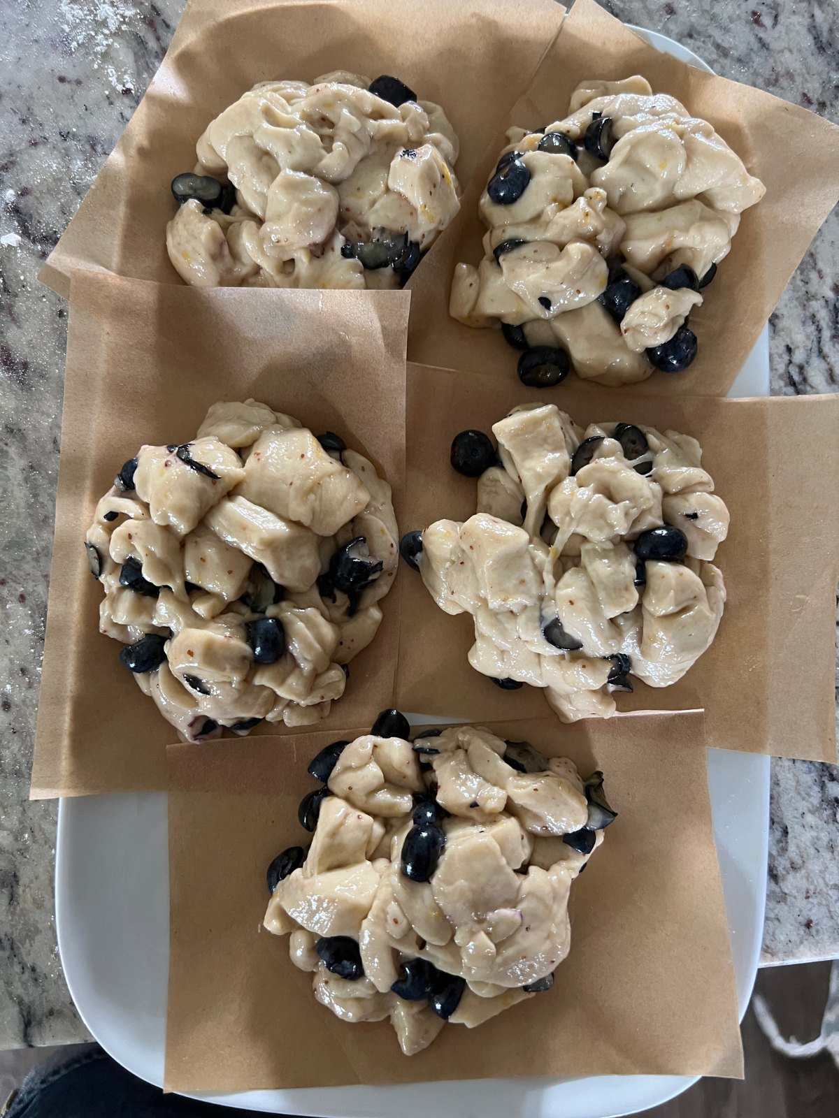 The sourdough blueberry lemon fritter doughs have been shaped into patties and sit on a parchment paper squares.