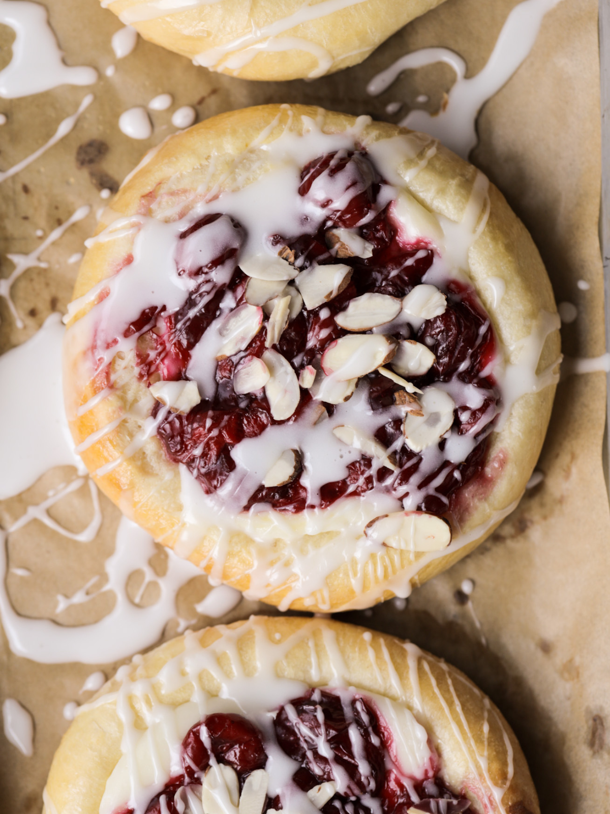 A closeup of the sourdough almond cherry cheesecake buns is shown with icing on a baking sheet.
