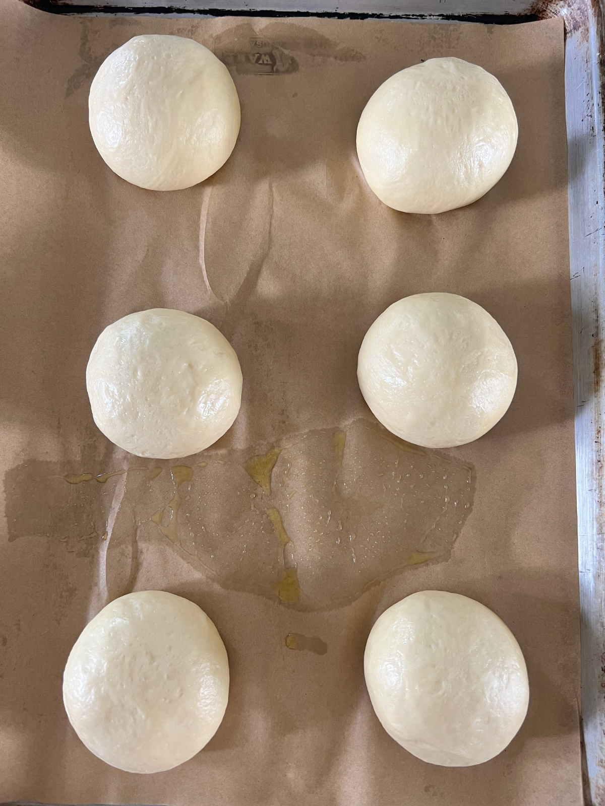 The sourdough brioche buns sit on a baking sheet after their second rise. They're ready to be shaped and filled.