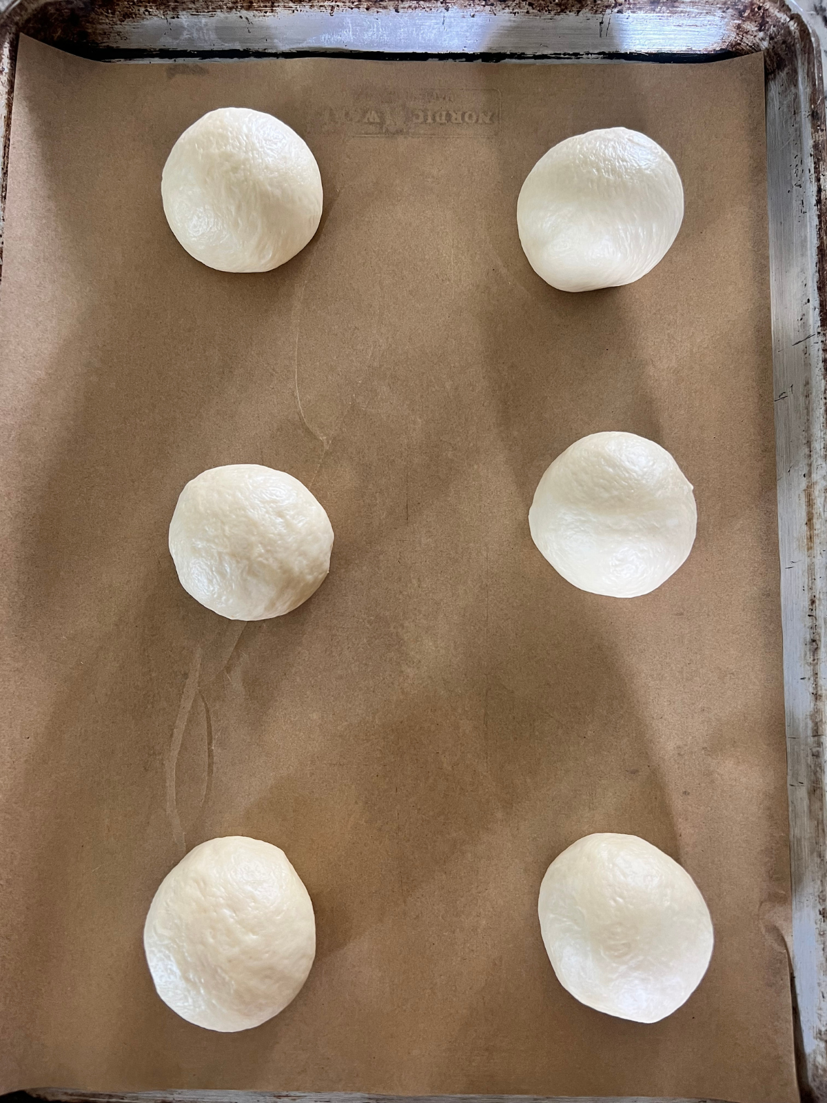 The divided dough balls sit on a parchment paper-lined baking sheet.