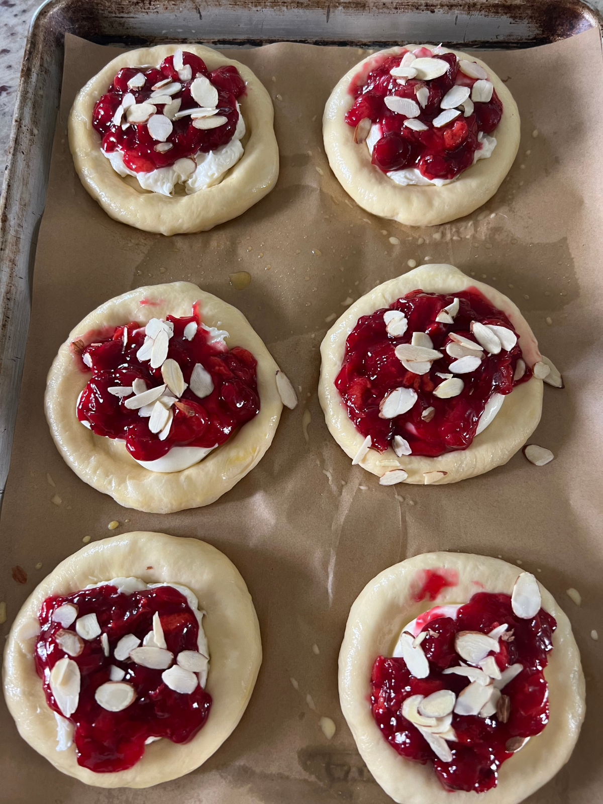 The sourdough cherry almond cream cheese buns have been brushed with egg wash, filled with cream cheese filling, cherry filling, and topped with slivered almonds.