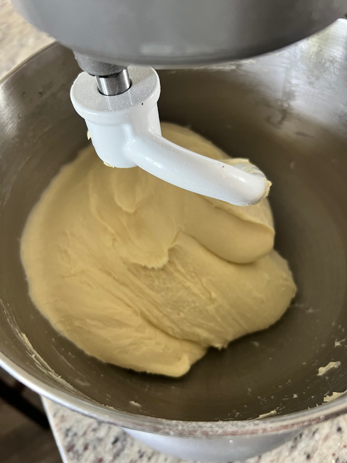 Sourdough brioche dough is shown being kneaded in a stand mixer with a dough hook attachment.
