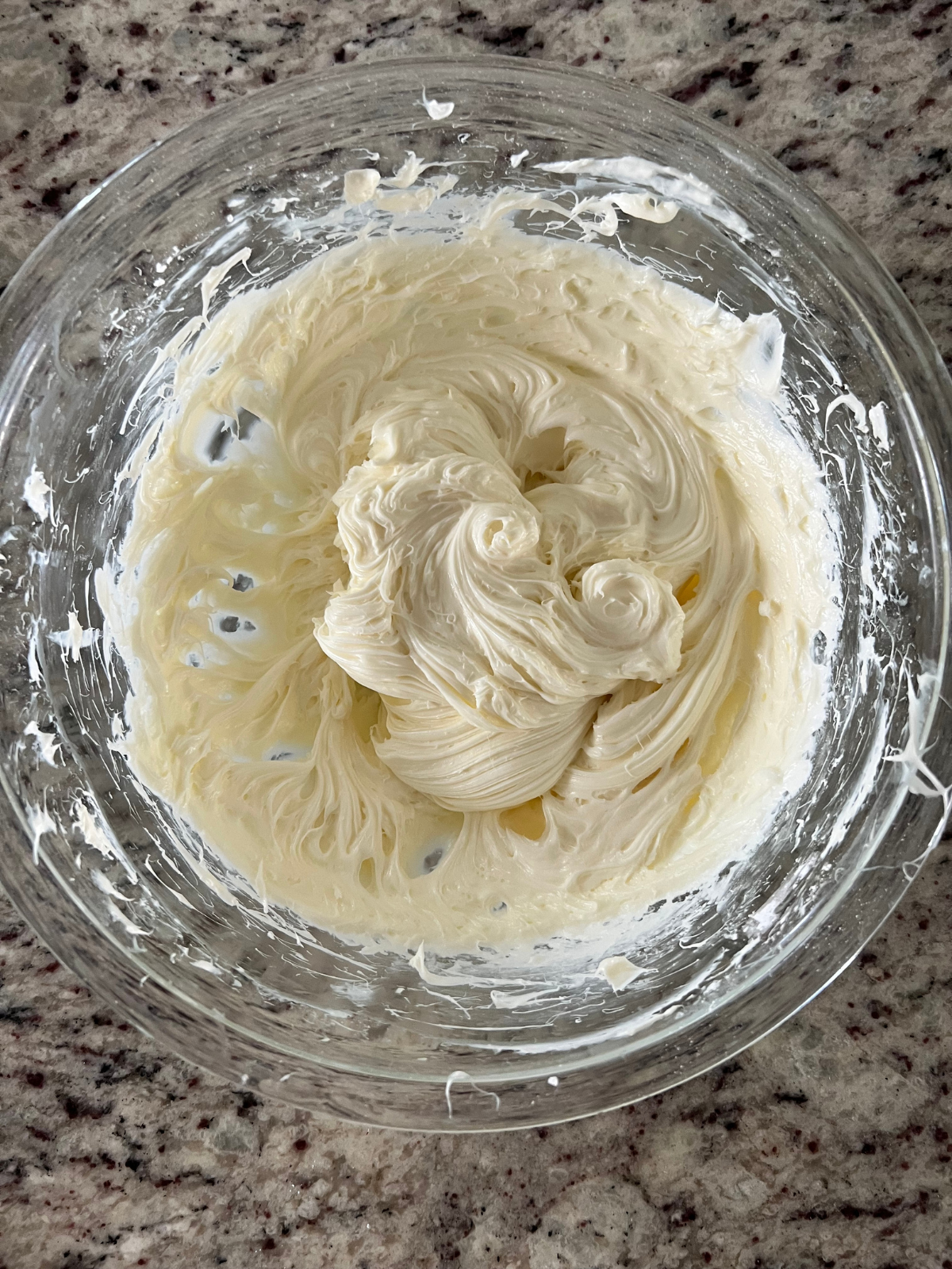 The cream cheese filling sits in a glass mixing bowl after being mixed together.