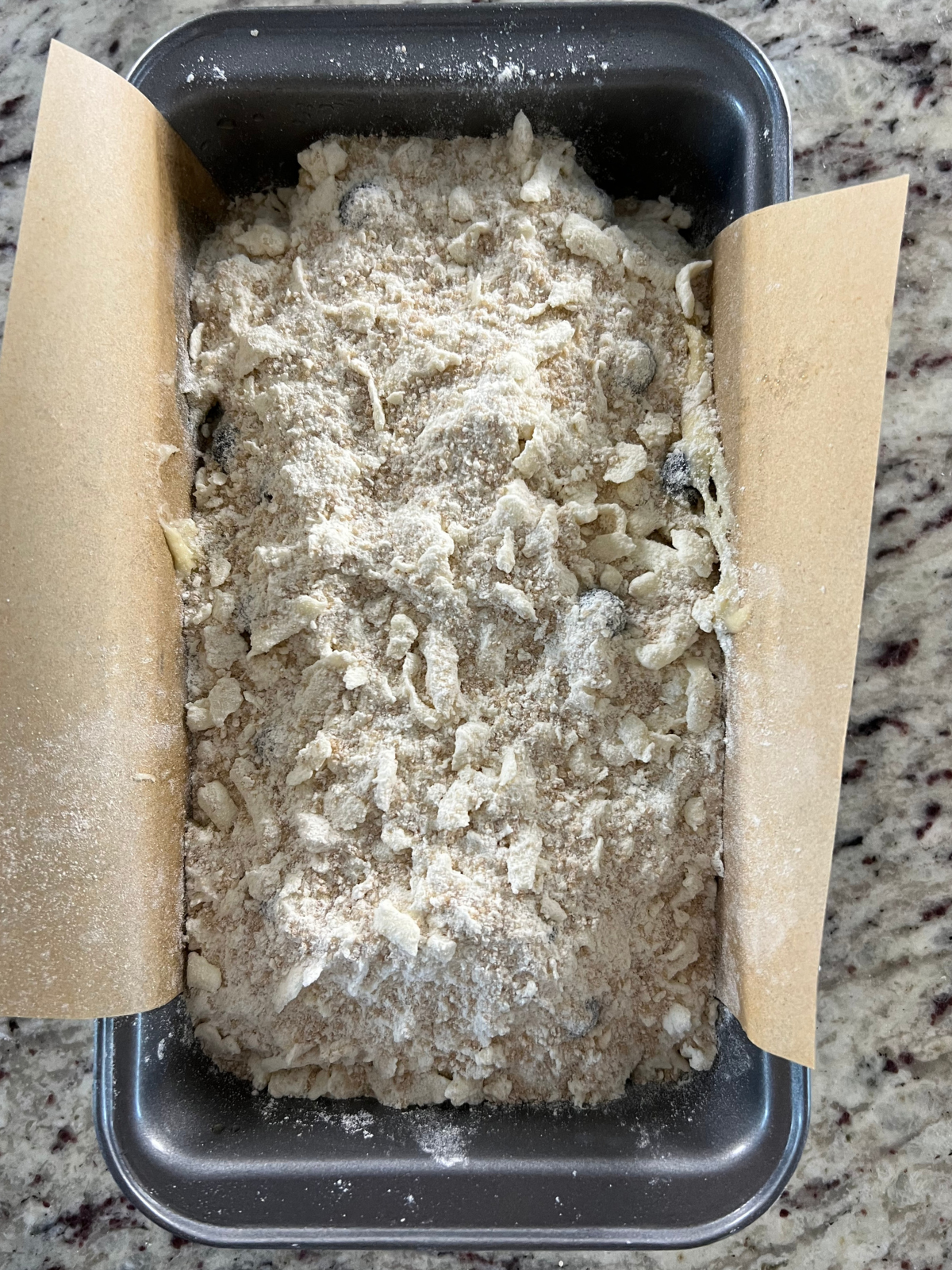 The sourdough discard blueberry crumble batter sits in a parchment paper lined loaf pan with the crumble over the top.