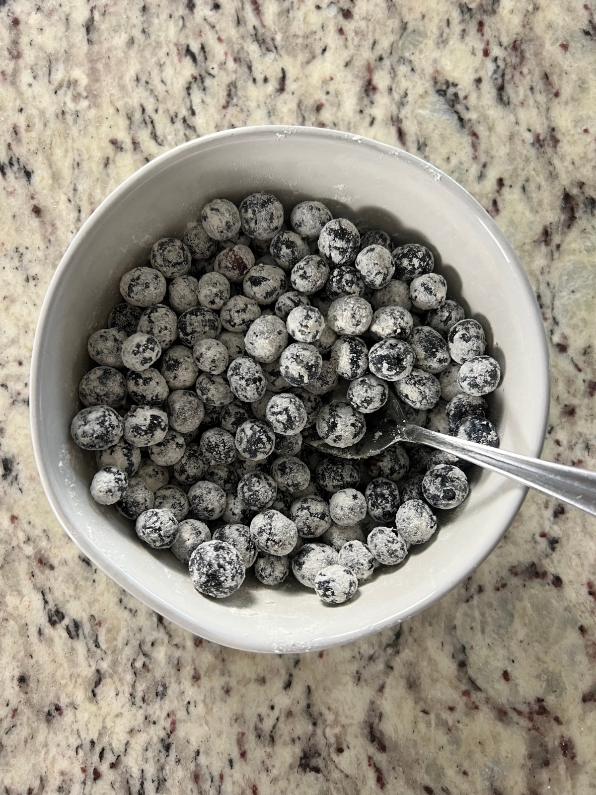 The blueberries sit in a bowl mixed with flour.